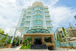 A multi-story hotel with a modern design, featuring a prominent entrance with glass doors and a curved roof. - Dao Ngoc Hotel (Phu Quoc)