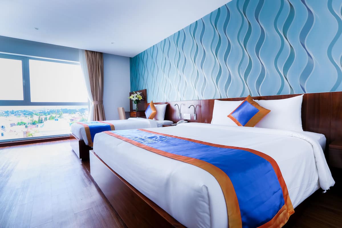 A hotel room with a large bed, a view of the city, and a wavy blue wall.