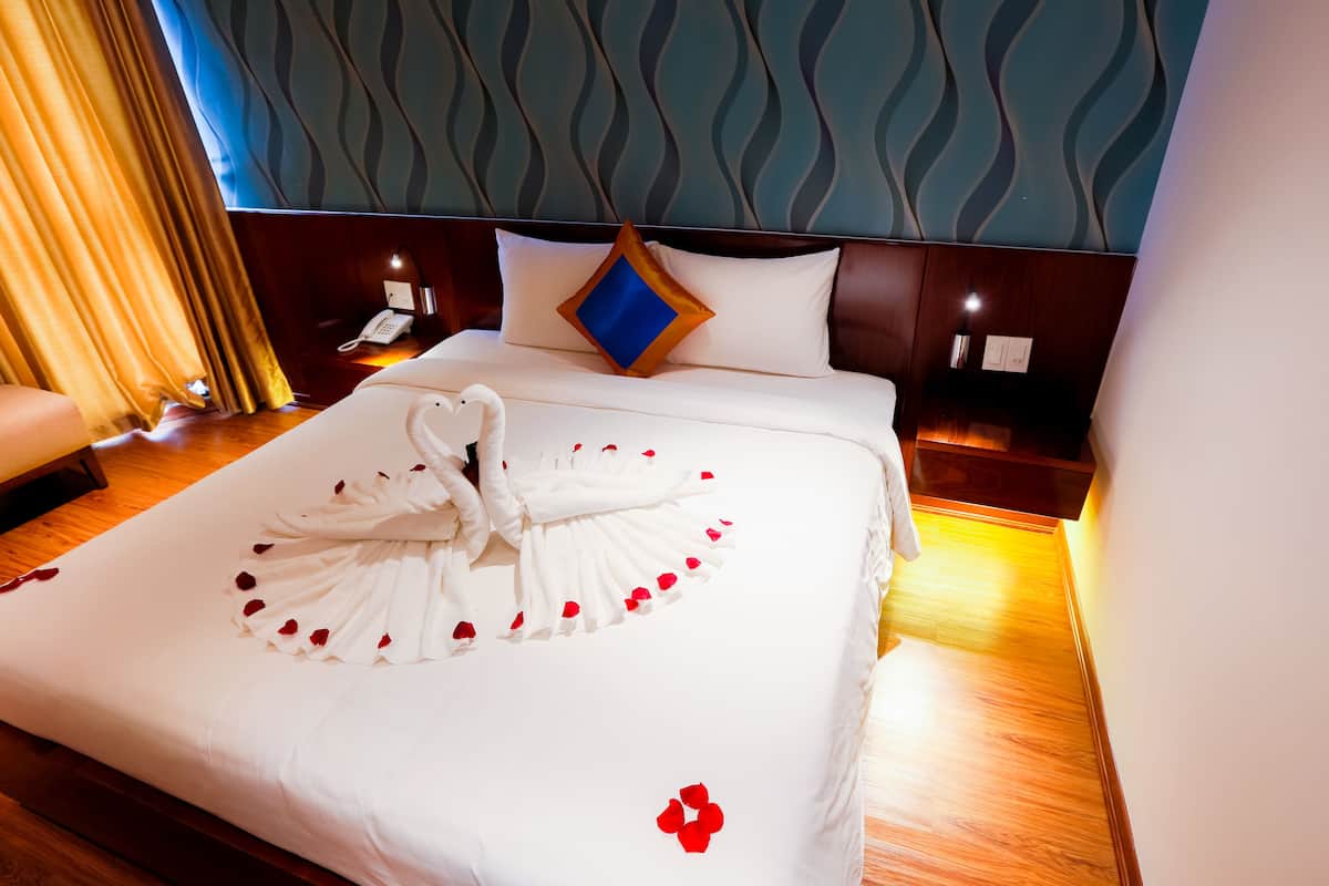 A hotel room with a neatly made bed, a bedside telephone, and a wall with a wavy pattern.