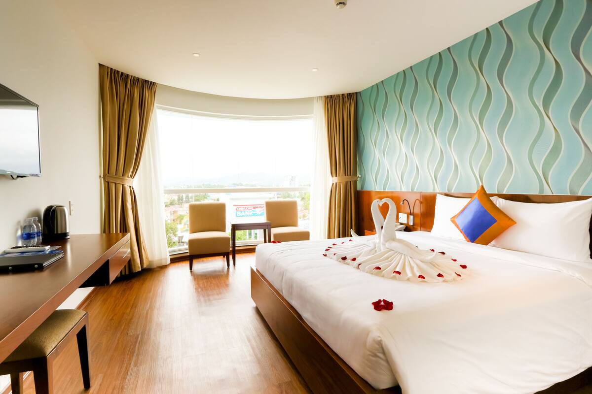 A hotel room with a large bed, a desk, a chair, and a view of the city.