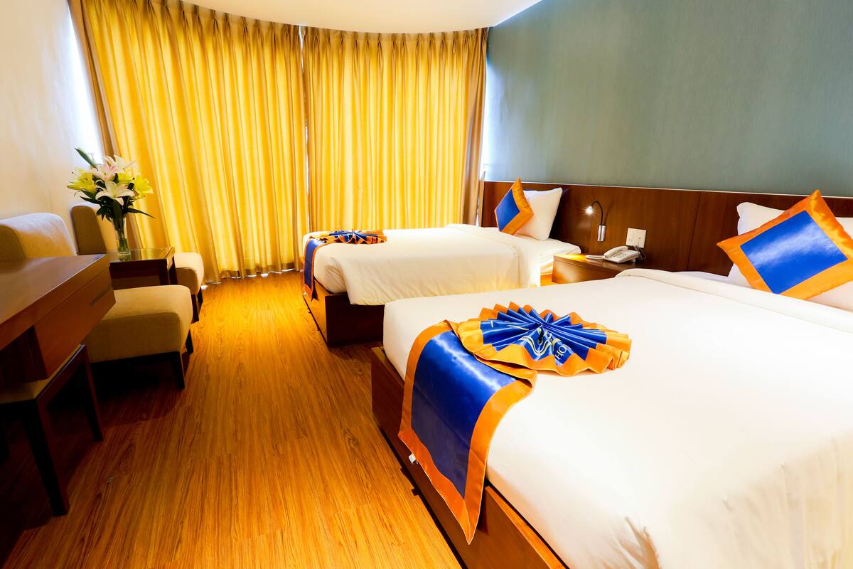 A hotel room with two beds, a desk, a chair, and a large window with curtains.