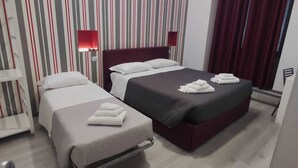 Habitación de hotel con dos camas, papel tapiz a rayas, cortinas rojas y una mesita de noche con lámpara.