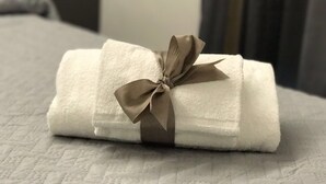 Una toalla blanca doblada con un lazo marrón, sobre un edredón con textura.