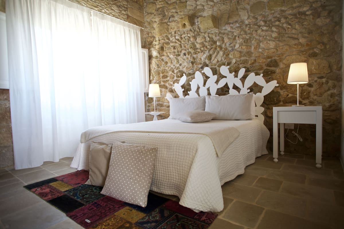 Ein Schlafzimmer mit einer Steinsäule, einem Bett mit weißer Bettwäsche, zwei Nachttischlampen und einem gemusterten Teppich.