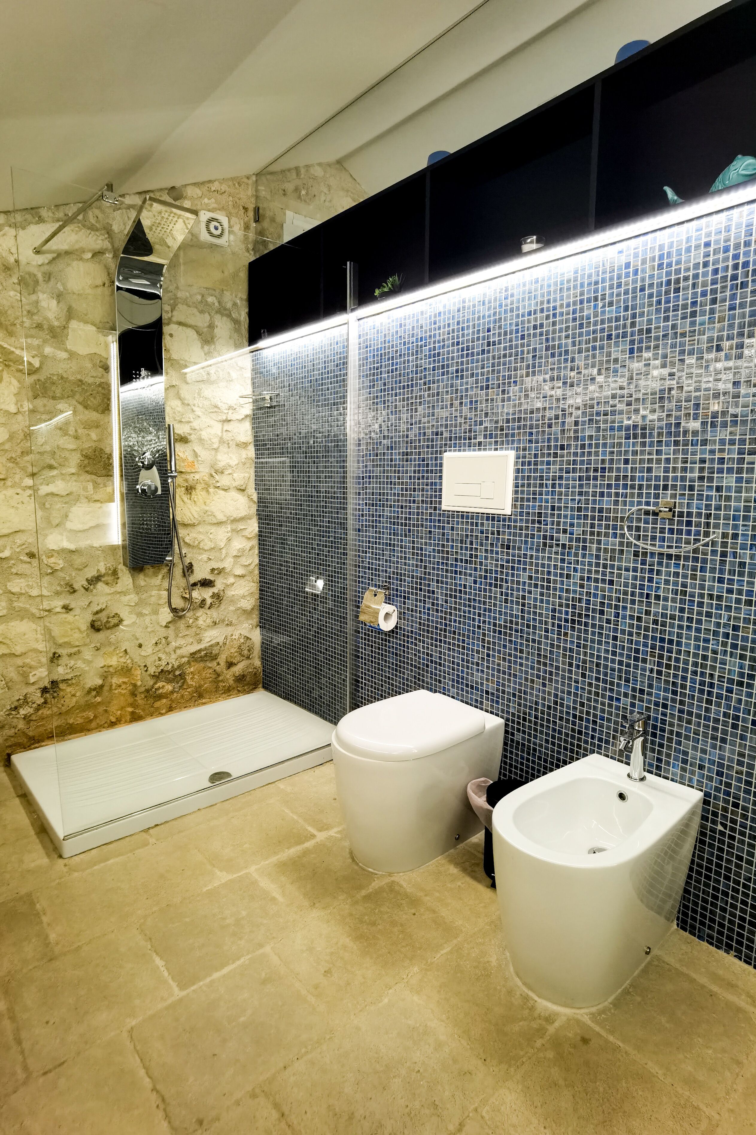 A bathroom with a stone wall, a shower, a bidet, and a sink.
