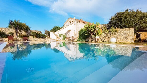 A clear swimming pool with a stone wall and a building in the background. - Don Agostino Relais Masseria (Martano)