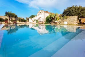 A clear swimming pool with a stone wall and a building in the background. - Don Agostino Relais Masseria (Martano)