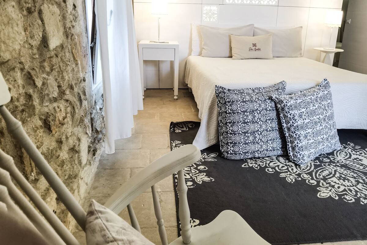 Ein Schlafzimmer mit Stewand, einem Bett mit gemusterten Kissen, einem Nachttisch und einer Wandleuchte.