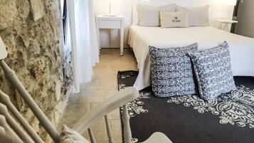 Une chambre avec un mur en pierre, un lit agrémenté d’oreillers à motifs, une table de chevet et un luminaire fixé au mur.