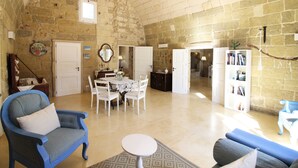 A spacious living area with a high stone ceiling, a dining table with chairs, a blue armchair, and a small round table. - Don Agostino Relais Masseria (Martano)