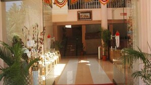 A hotel lobby with a red carpet, potted plants, and a staircase leading to an upper level. - The Kingdom (Port Blair)