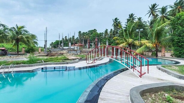 A swimming pool with a red bridge, surrounded by palm trees and greenery. - The Kingdom (Port Blair)