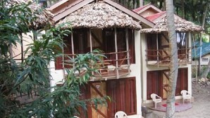 A bungalow with a thatched roof, wooden balconies, and a veranda with plastic chairs. - The Kingdom (Port Blair)