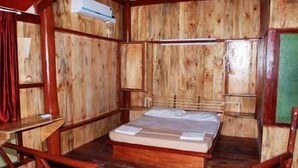 A wooden room with a bed, a table, and an air conditioning unit. - The Kingdom (Port Blair)