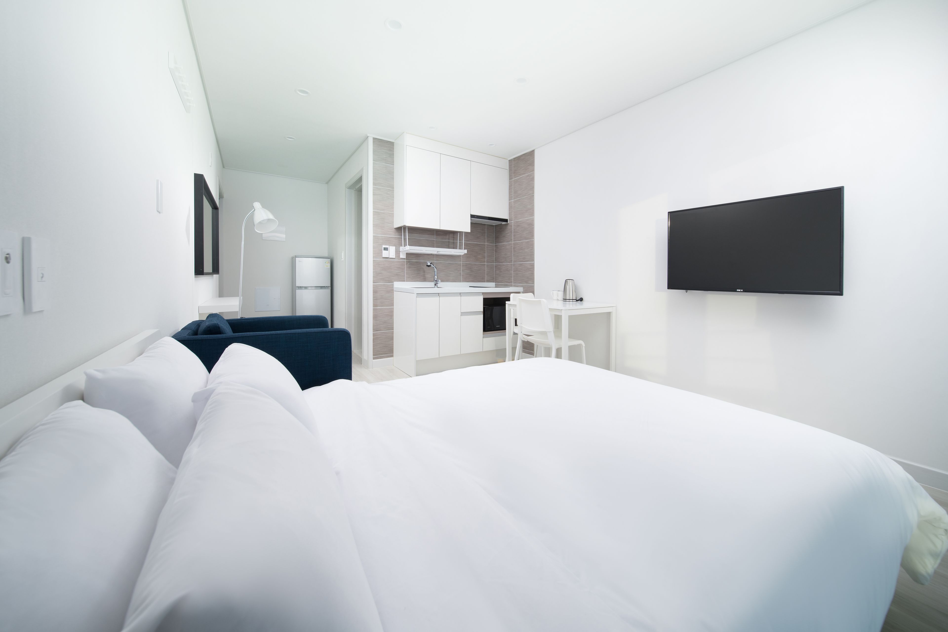 A modern hotel room with a large bed, a desk, and a kitchenette.