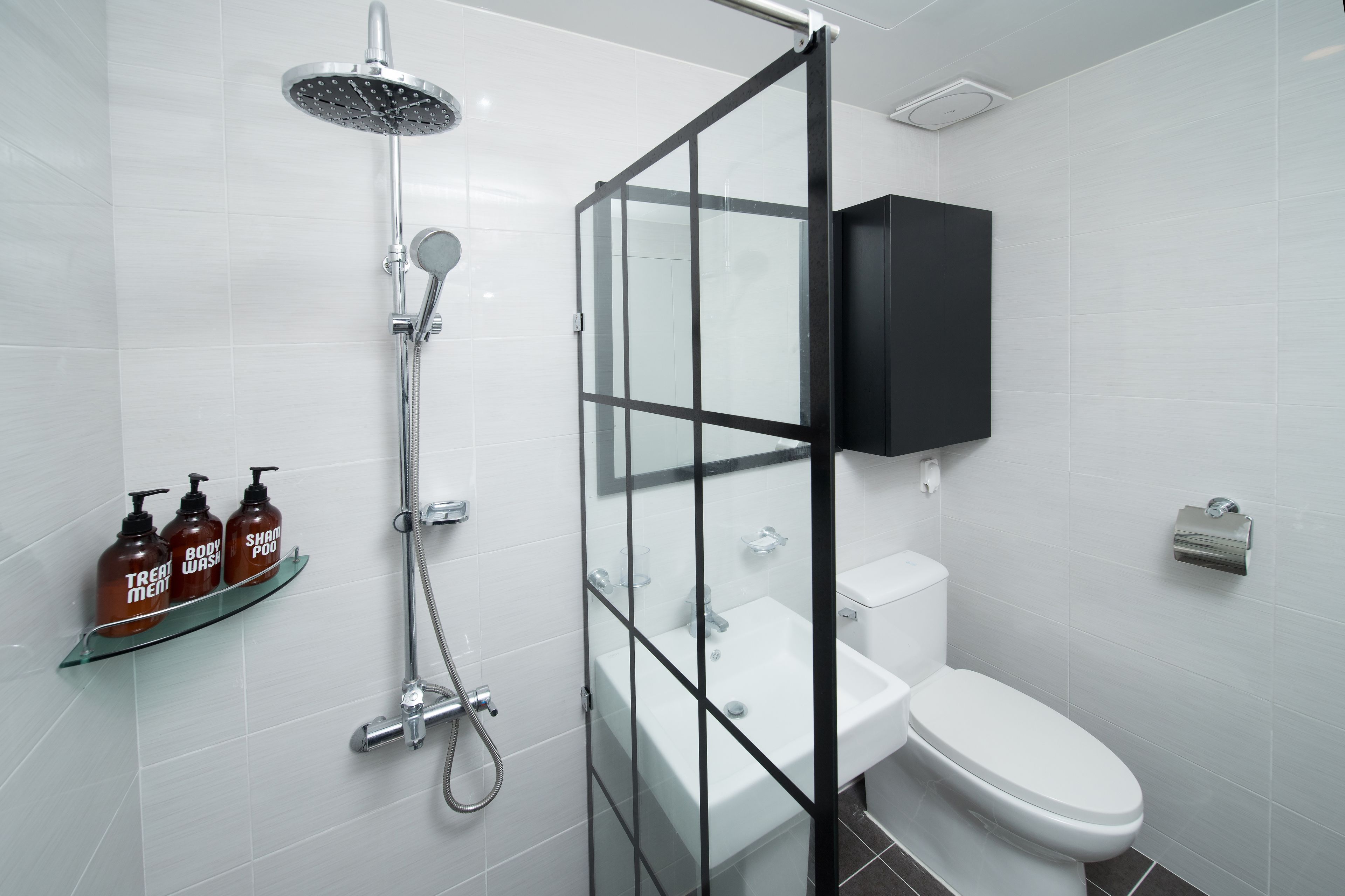Un baño moderno con cabina de ducha de vidrio, inodoro blanco y botiquín negro.
