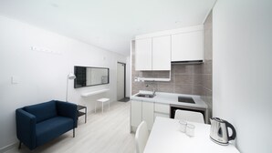 A modern, compact kitchen with white cabinetry, a small dining table, and a blue sofa. - Soo Pension (Seogwipo)