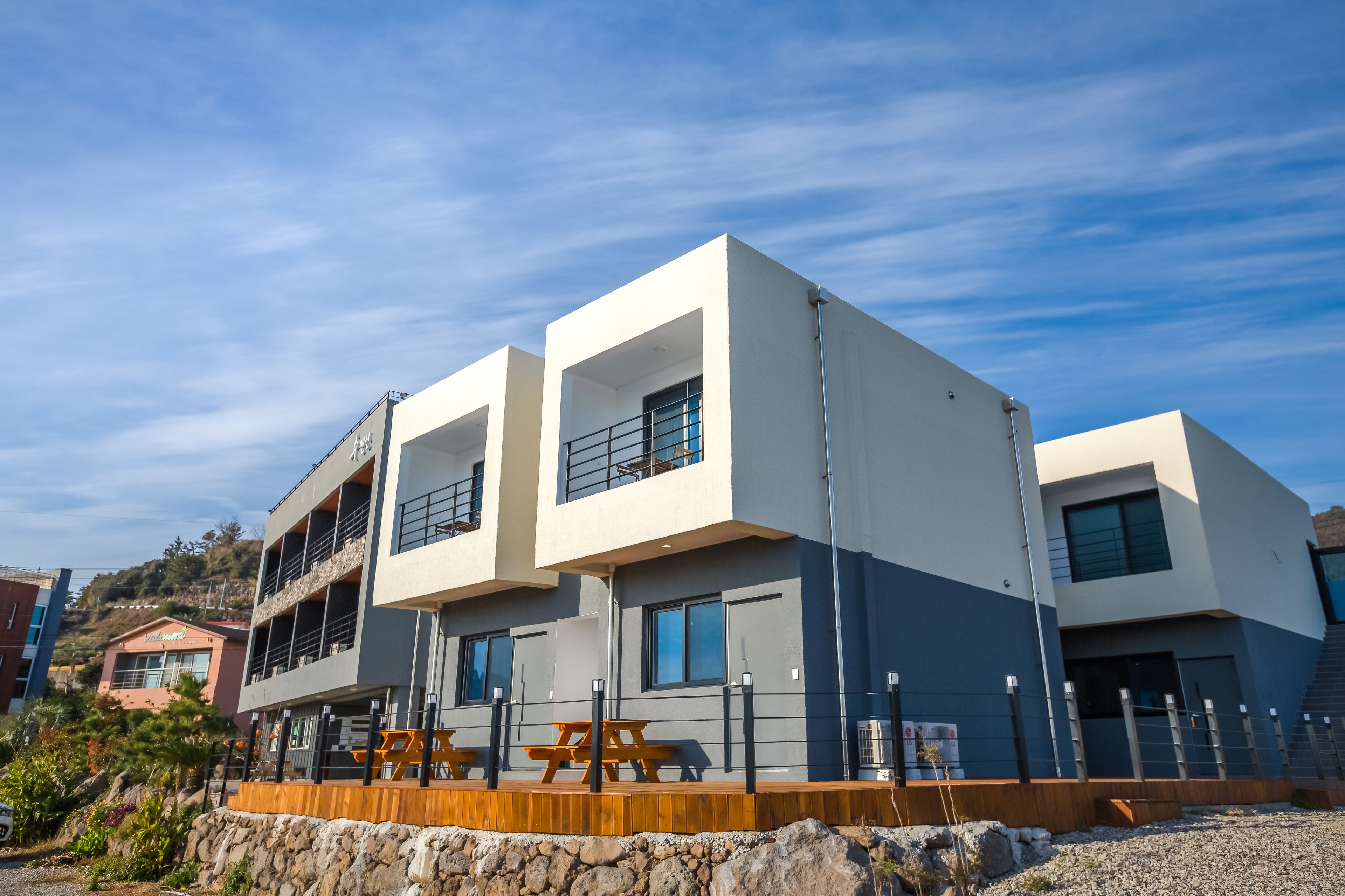 A modern multi-story building with a stone retaining wall, wooden picnic tables, and a clear blue sky.