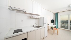 A modern kitchen with white cabinets, a built-in dishwasher, and a window with a view. - Soo Pension (Seogwipo)