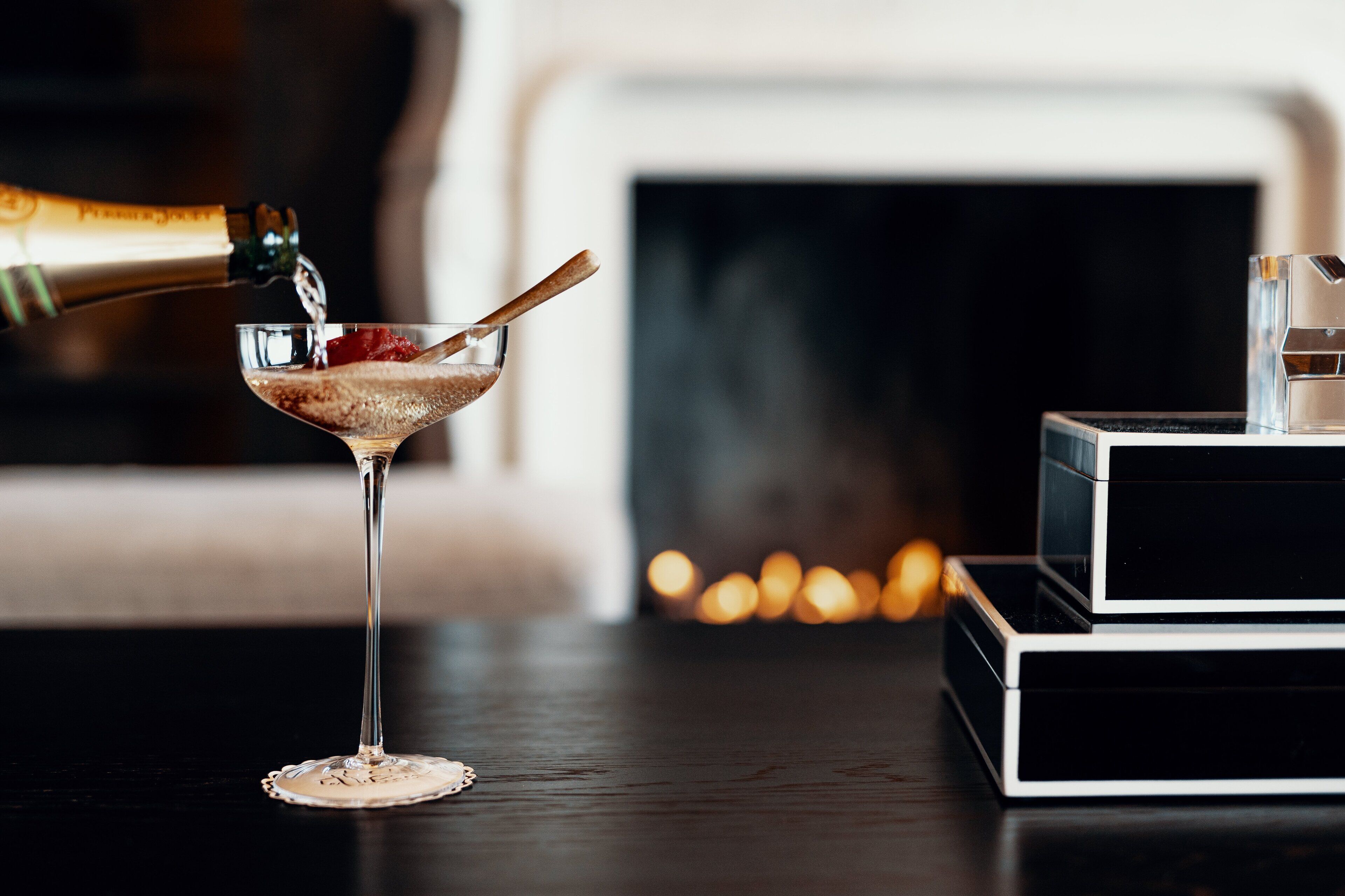 A martini glass on a table with a bottle of champagne being poured into it.