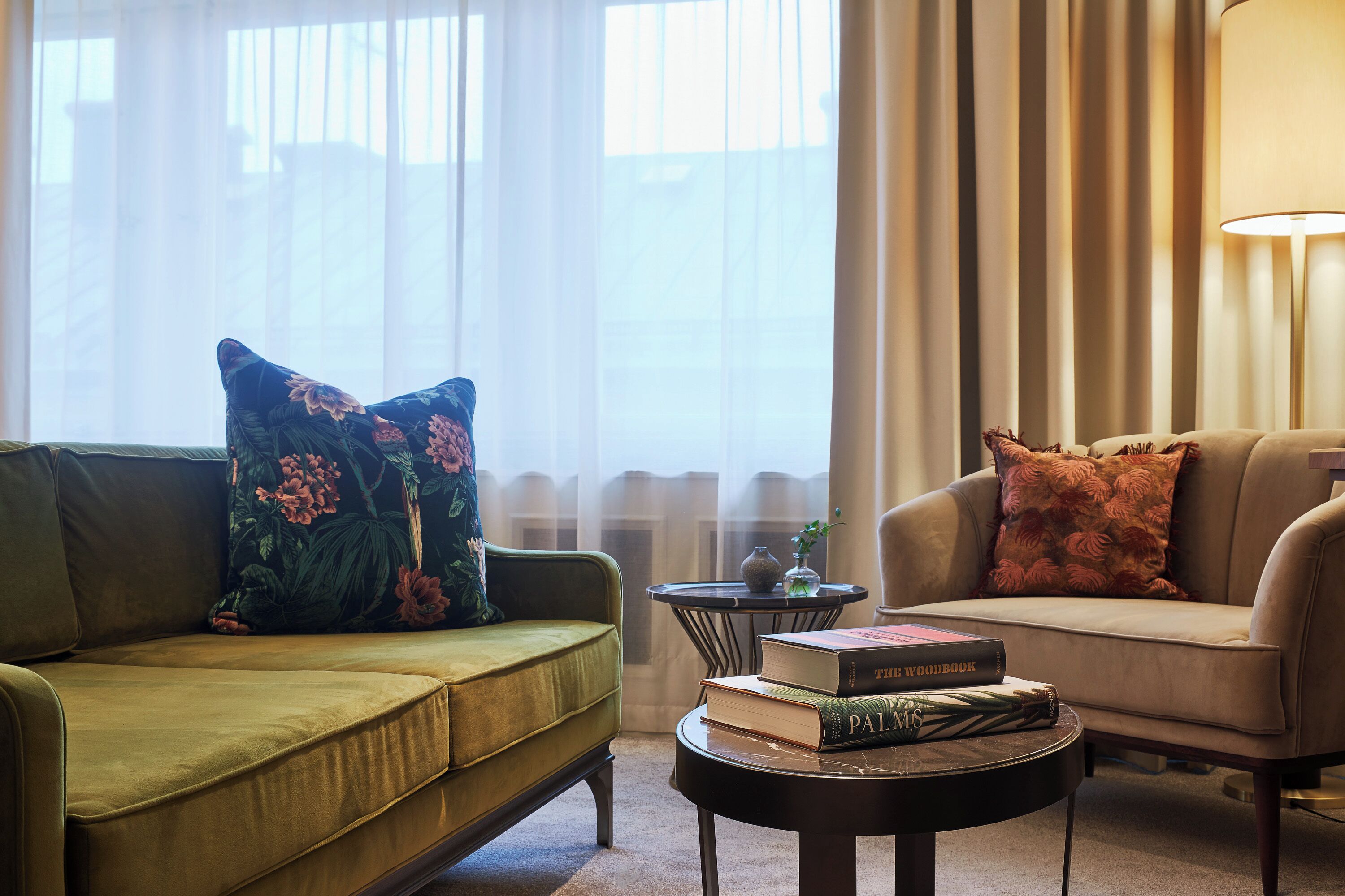 A living room with a green sofa, a beige armchair, a round coffee table with books, and a lamp.