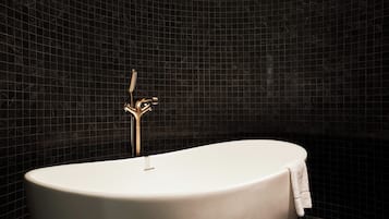 A modern bathroom with a freestanding bathtub, a gold faucet, and a towel on the side.