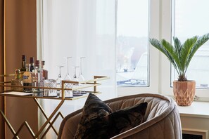A room with a window, a table with bottles and glasses, a chair with a cushion, and a potted plant.