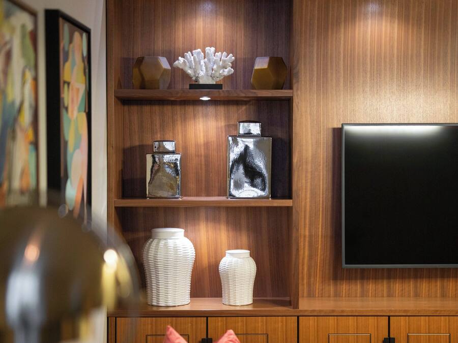 Una sala de estar moderna con un sofá de cuero, un televisor de pantalla plana, estanterías de madera con objetos decorativos y un suelo con patrón de espiga.