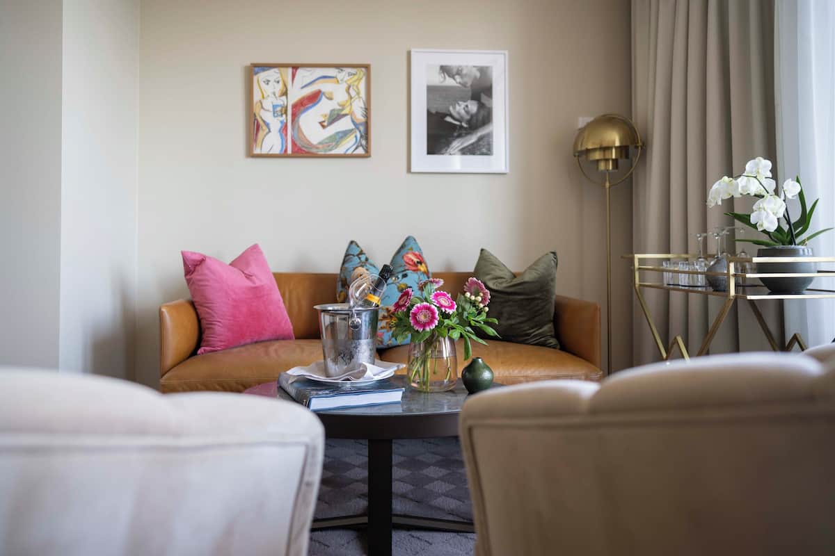 A modern living room with a leather sofa, a coffee table with books and flowers, and a gold floor lamp.