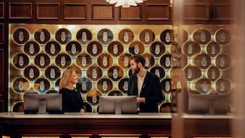 A reception desk with a check-in counter, a patterned wall with circular designs, and a chandelier above.