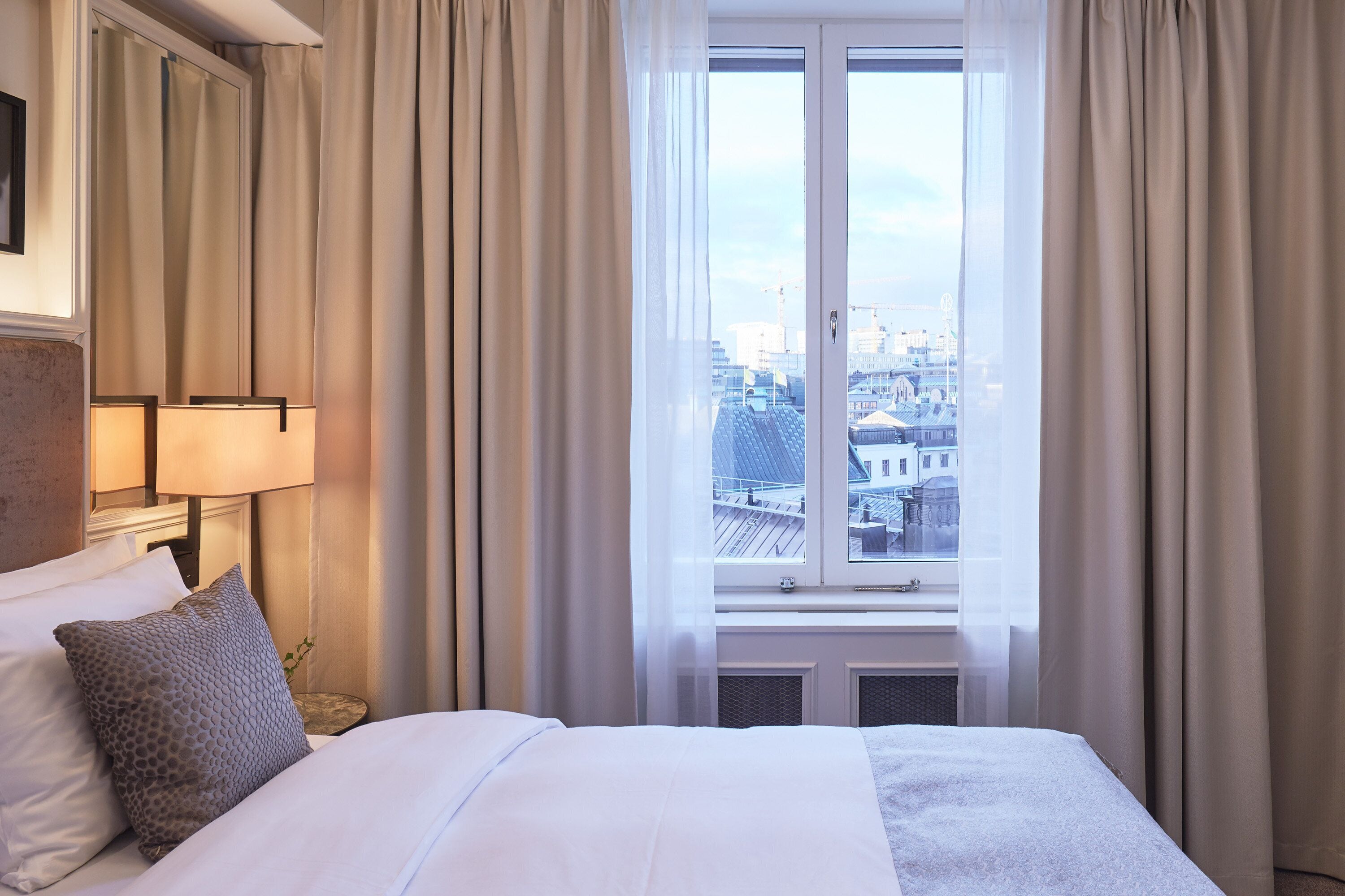 A hotel room with a bed, a nightstand, a lamp, and a window with curtains.