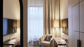 A hotel room with a large window, a sofa, a small round table, a desk, and a TV.