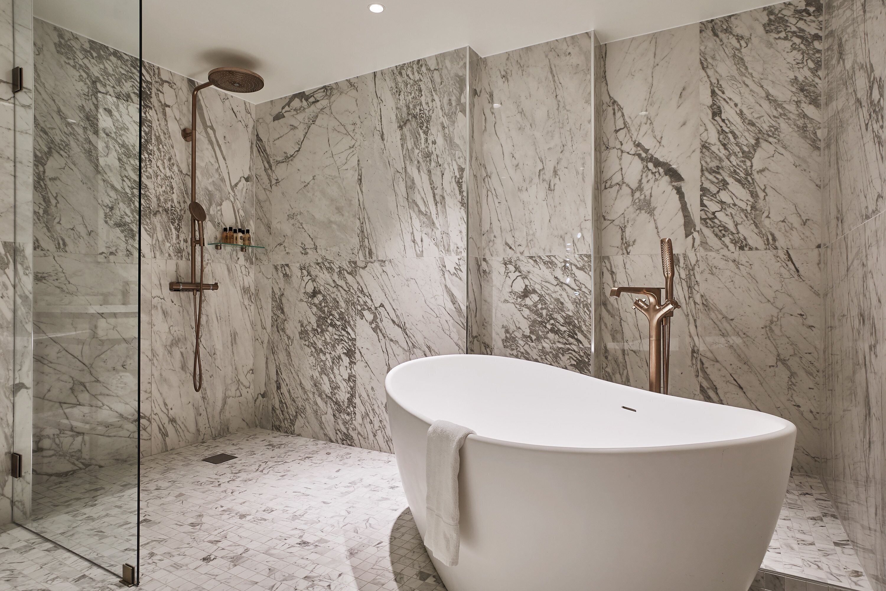 A modern bathroom with a freestanding bathtub, a glass-enclosed shower, and marble walls.