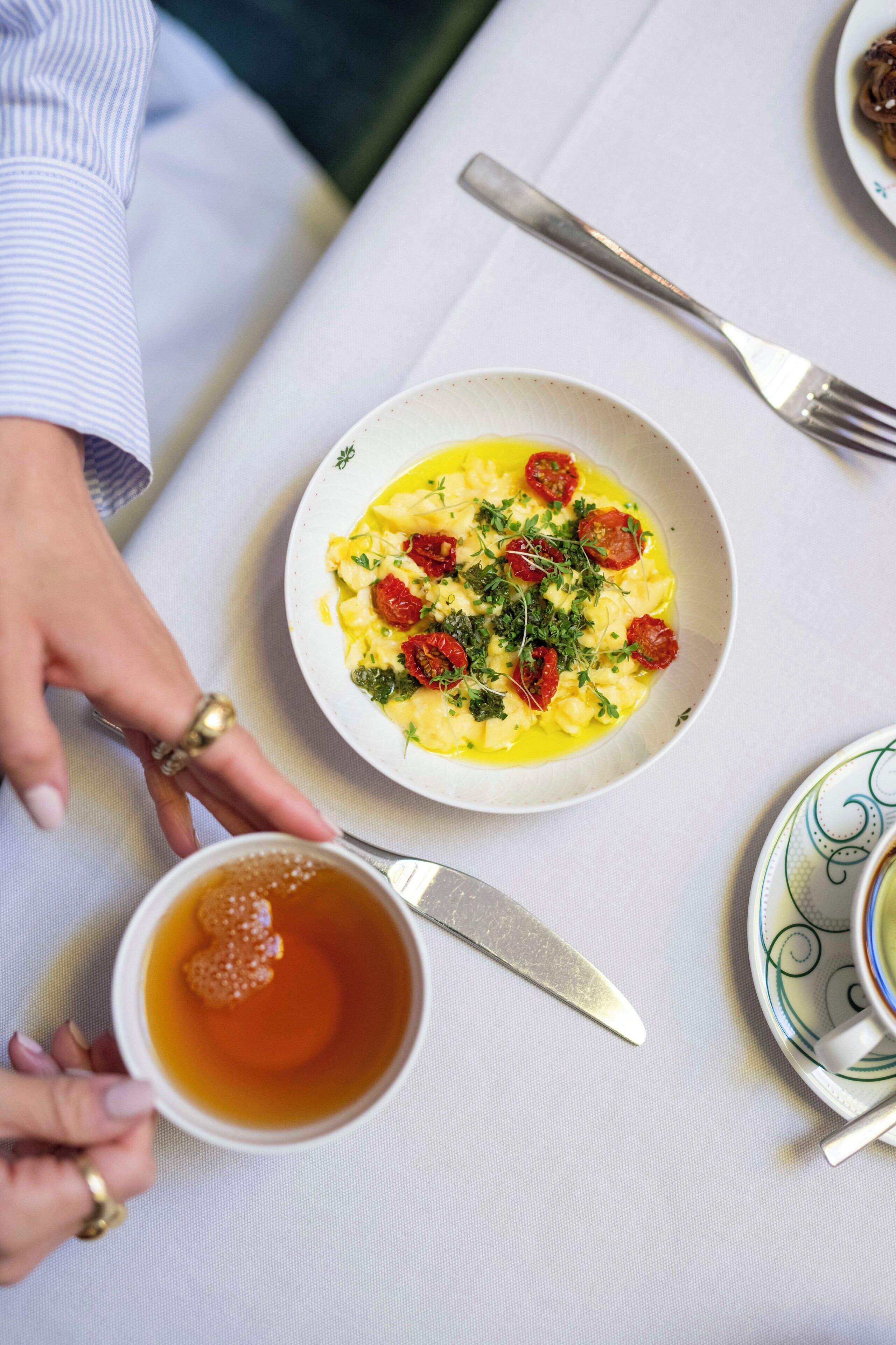 Una mesa servida con un plato de comida, una taza de té y un tenedor.