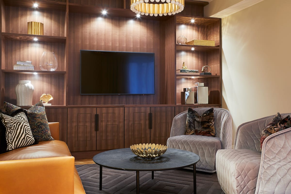 A modern living room with a large flat-screen TV, wooden shelving, and comfortable seating.
