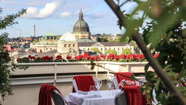 A terrace with tables set for dining, overlooking a cityscape with a prominent dome and red flowers. - Bank Hotel, a member of Small Luxury Hotels of The World (Stockholm)