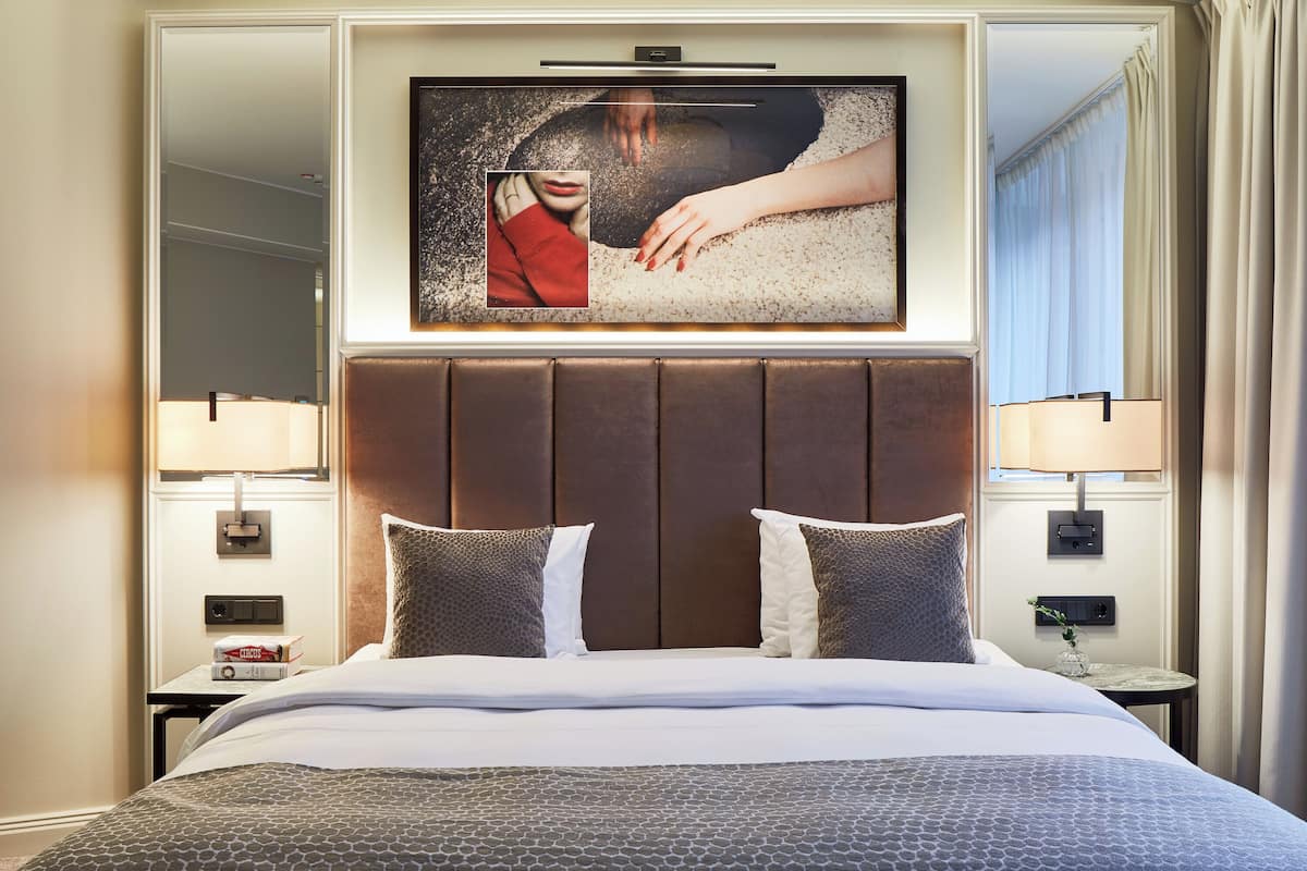 A hotel room with a large bed, two bedside tables, a mounted TV, and a window with curtains.