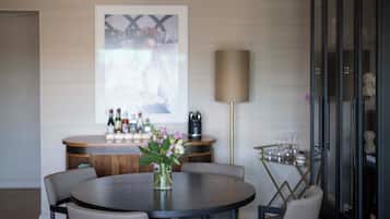 Un comedor moderno con una mesa redonda, seis sillas, un jarrón con flores, una barra con botellas y copas, y un cuadro grande en la pared.