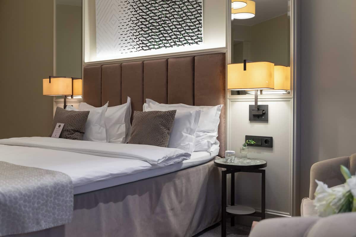 A hotel room with a large bed, two bedside lamps, a small table with a glass, and a chair.