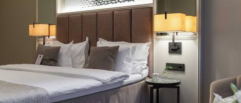 A hotel room with a large bed, two bedside lamps, a small table with a glass, and a chair.