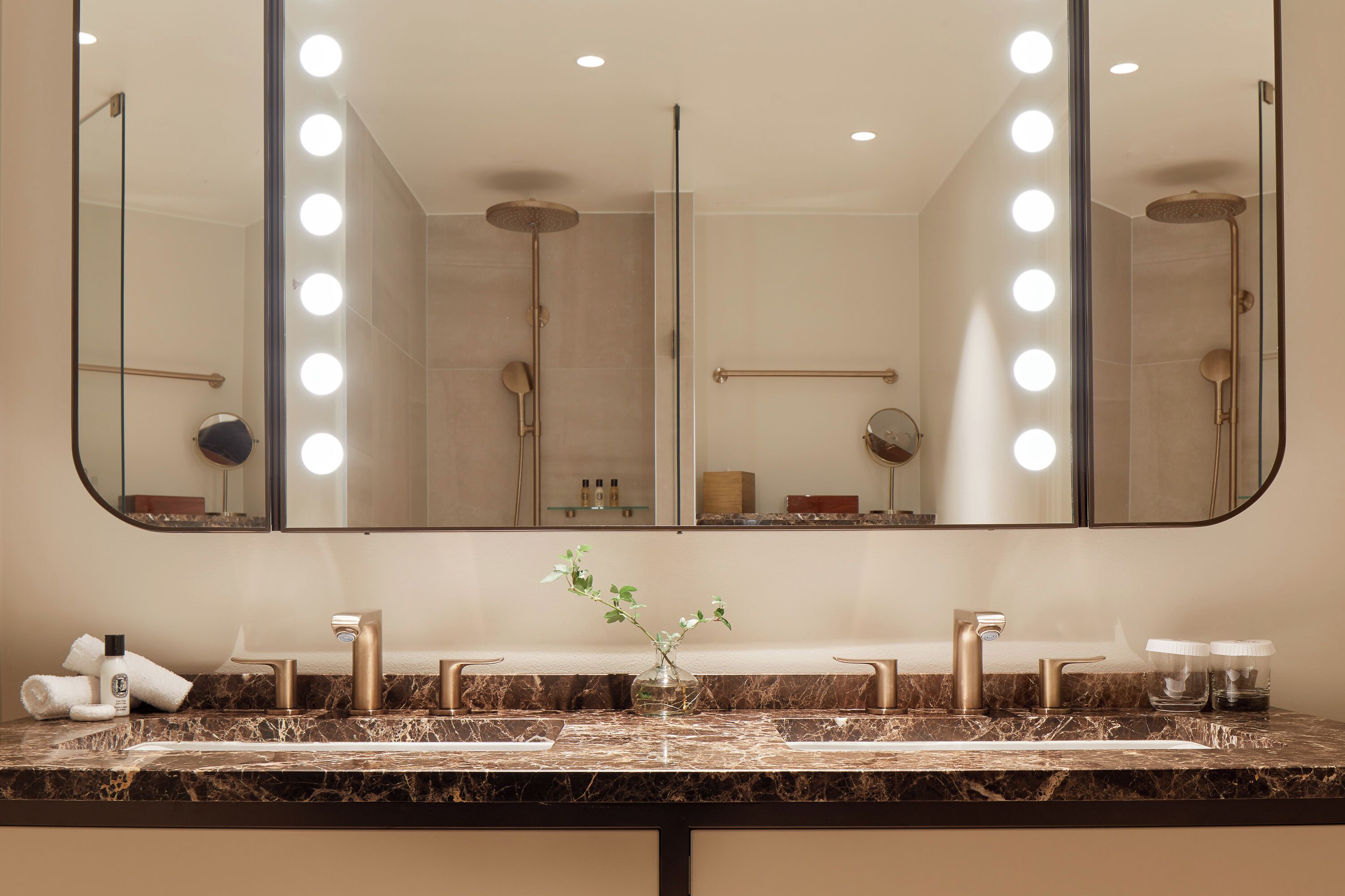 A bathroom with a large mirror, multiple lights, a marble sink, and a towel rack.