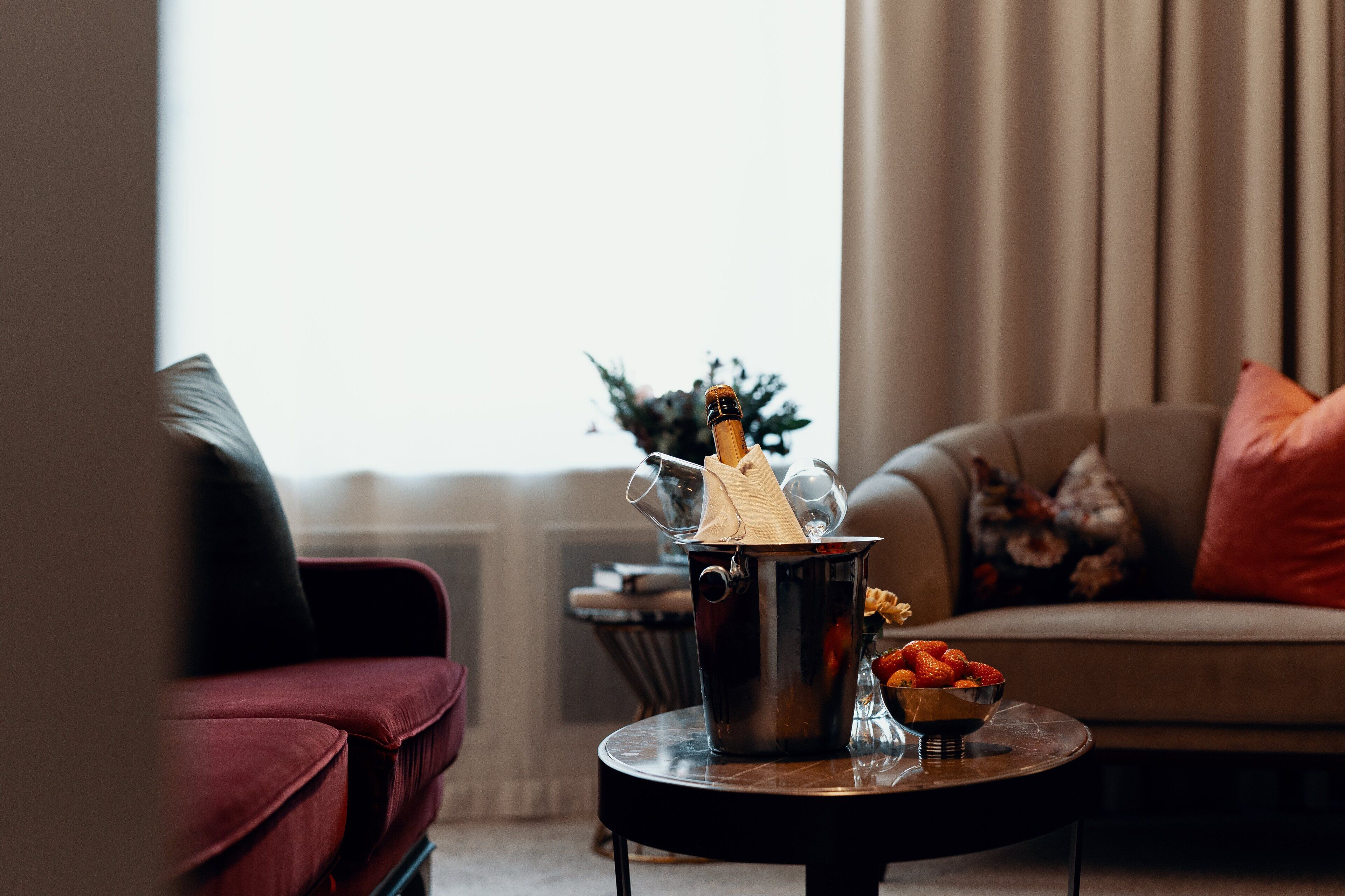 A living room with a red sofa, a round coffee table with a fruit bowl and a champagne bucket.