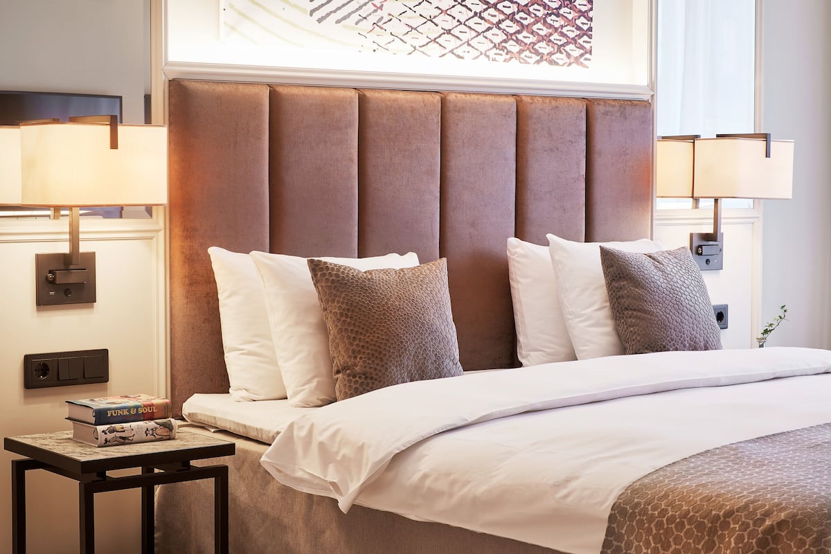 A neatly made bed with a padded headboard, two bedside lamps, and a small table with a book.
