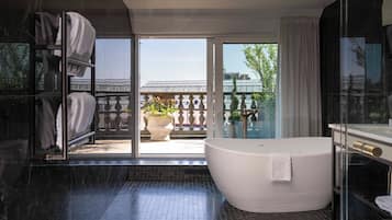 A modern bathroom with a large bathtub, a glass shower enclosure, and a view of a balcony with potted plants.