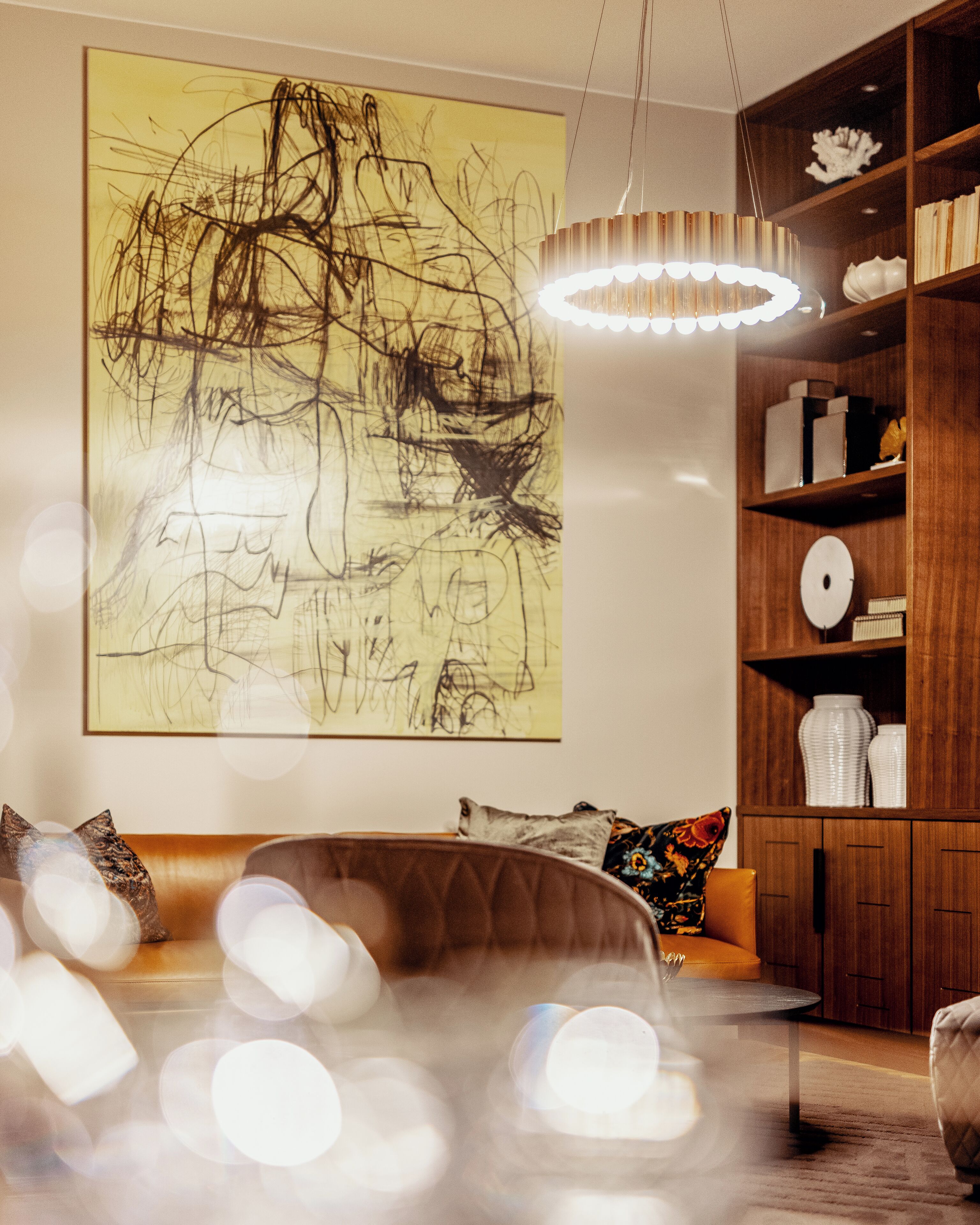 A living room with a large abstract painting, a wooden bookshelf, and a leather sofa.