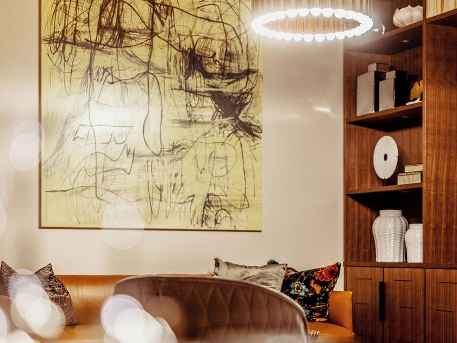 Una sala de estar con un cuadro abstracto grande, una estantería de madera y un sofá de cuero.