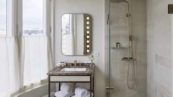 Un baño con tocador, espejo con iluminación, ducha y vistas de la ciudad.