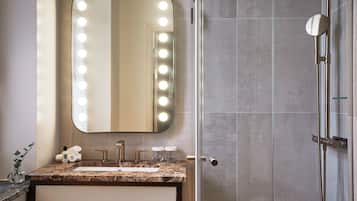 Un baño con tocador, espejo con luces, ducha y paredes de azulejos.