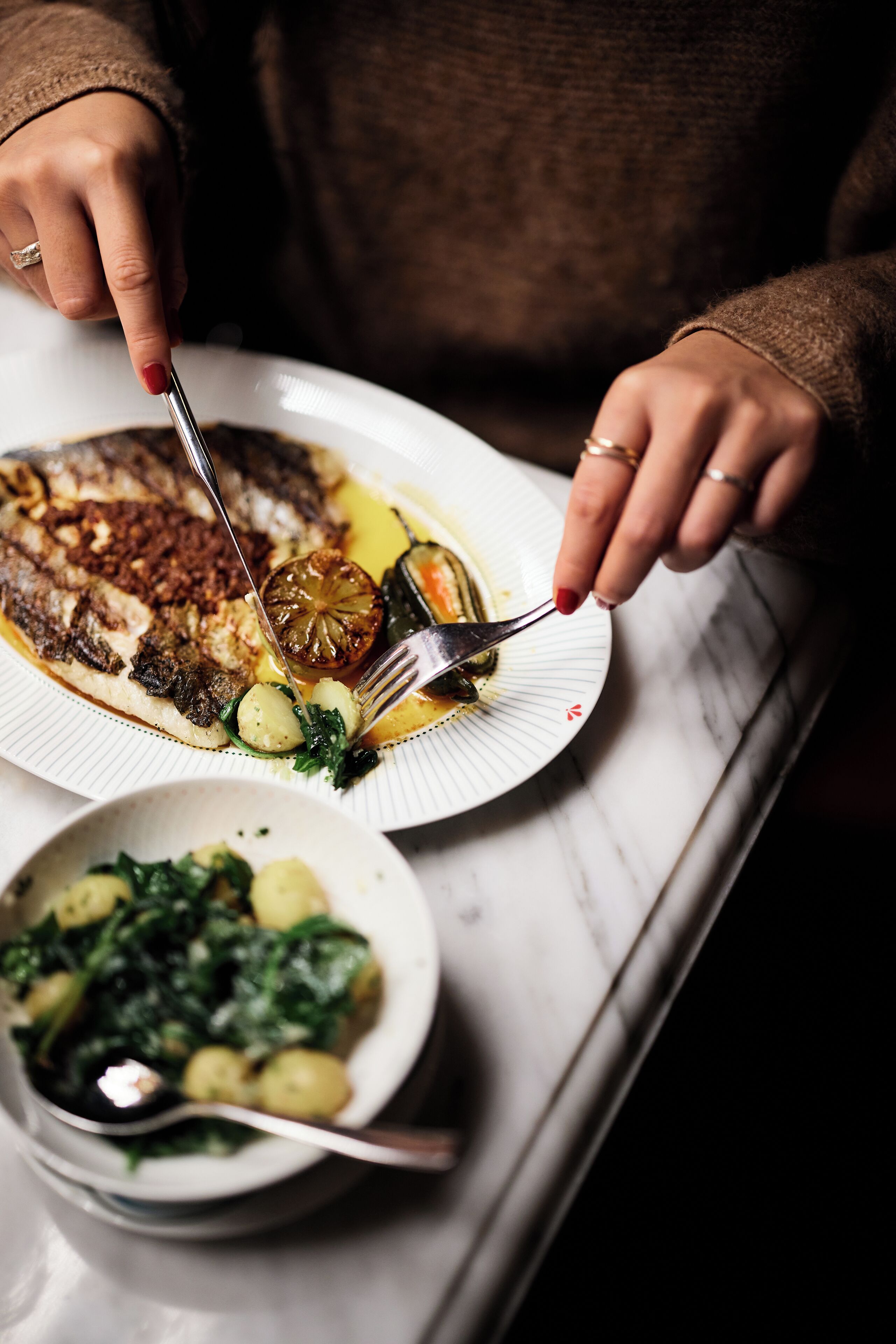 A person serving a meal with a fish, vegetables, and a small bowl of greens.