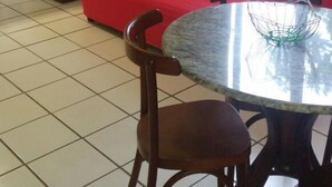 A living area with a red sofa, a round table with a wire basket, and a kitchen in the background. - Residencial Salinas (Florianópolis)